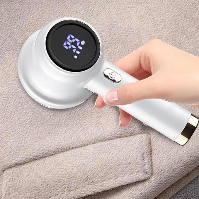 Mano usando quitapelusa eléctrico sobre suéter gris extendido en mesa de madera